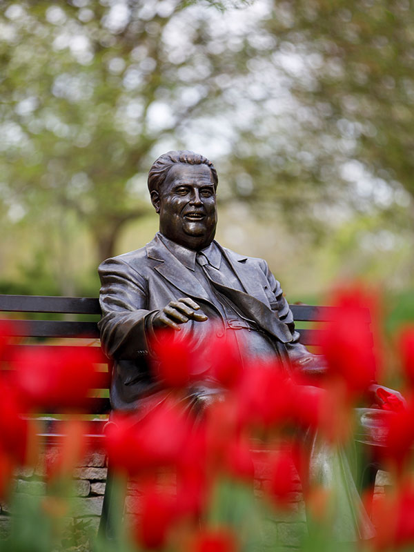 A photo of the Herman B Wells statue on campus, surrounded by blooming red tulips.