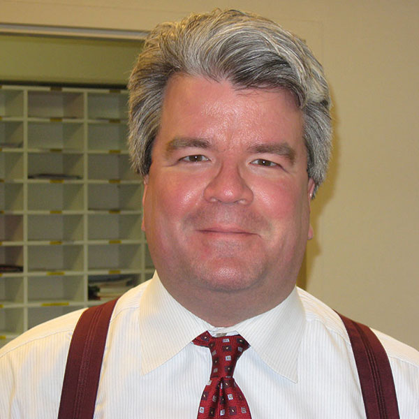 Steve DeBrota poses in an office and wears a white dress shirt and suspenders.
