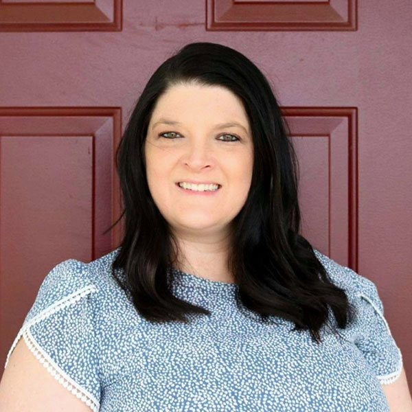 Heather Andress poses in front of a red door and wears a blue and white shirt.