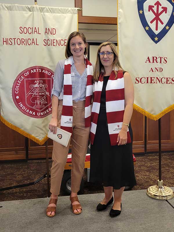 Two faculty members pose beside departmental and College banners.