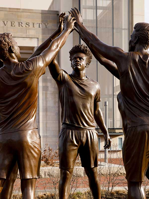 A bronze statue of four students raising their hands together.