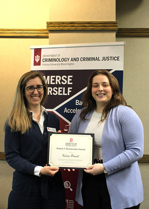 A photo of two women smiling and holding a certificate labeled “Robert F. Borkenstein Award.” They stand in front of a departmental banner for Criminology and Criminal Justice at Indiana University Bloomington.
