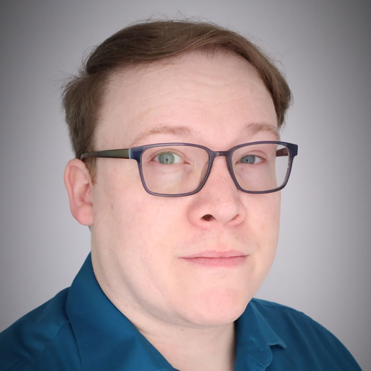 A headshot of Brian Ledbetter, who wears a teal shirt and and smiles slightly at the camera with a neutral backdrop.